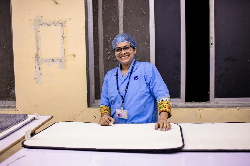 A cheerful healthcare worker in scrubs with a badge, standing confidently in a hospital room.